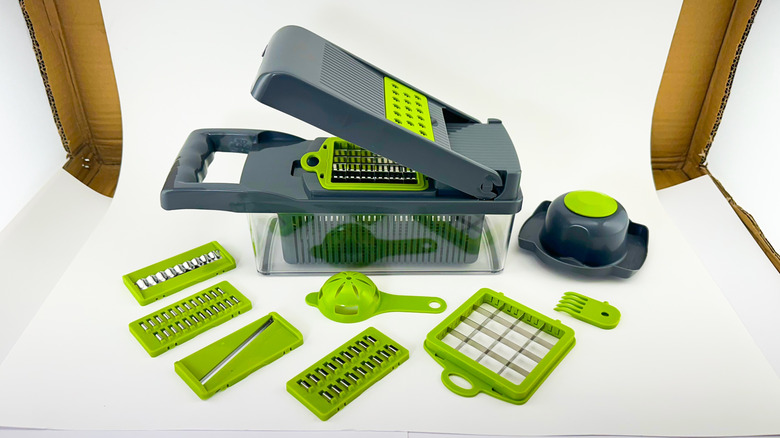 A grey and green vegetable chopper with all its accessories laid out