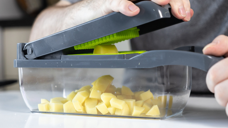 Hands using a grey plastic vegetable chopper with diced potatoes underneath