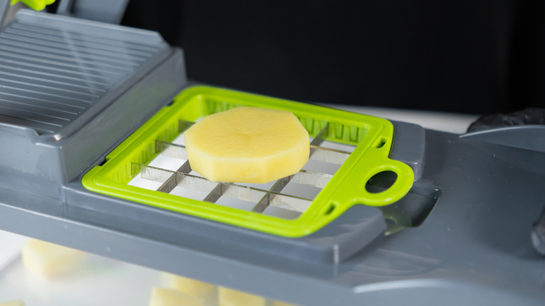 A slice of peeled potato sits on the blades of a vegetable chopper