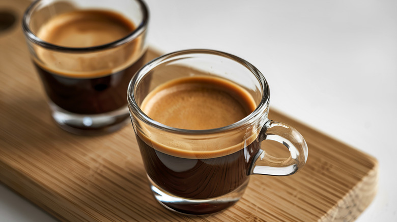 Two espressos in glass cups, resting on wooden tray