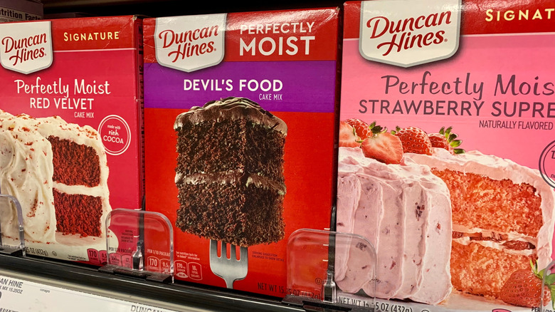 Boxes of Duncan Hines cake mix on store shelves, including red velvet, Devil's Food, and strawberry flavors