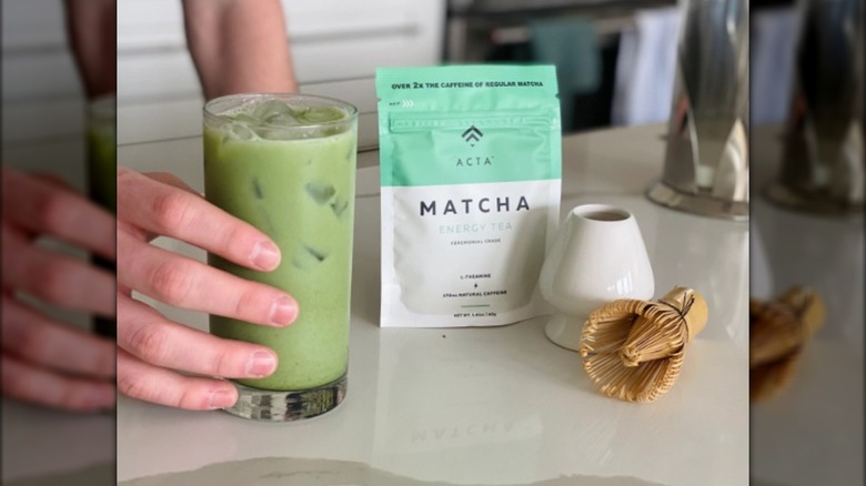 A hand holding a glass of Acta Matcha tea.