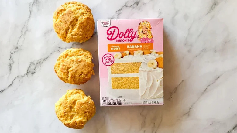 A box of Dolly Parton's banana cake mix on a marble countertop next to some cupcakes
