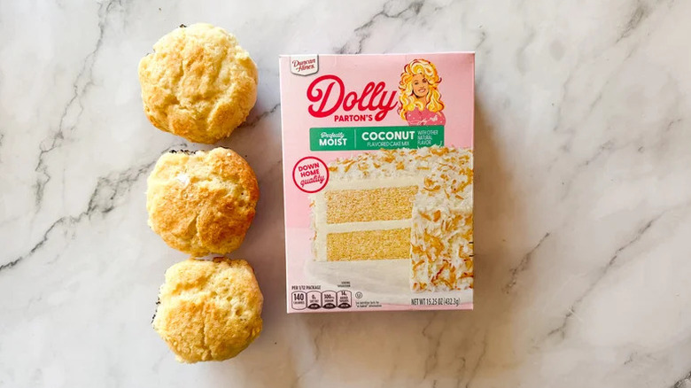 A box of Dolly Parton coconut cake mix on a marble table top next to three cupcakes