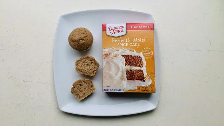 A box of Duncan Hines Signature Perfectly Moist Spice Cake sitting on a square white plate next to cupcakes