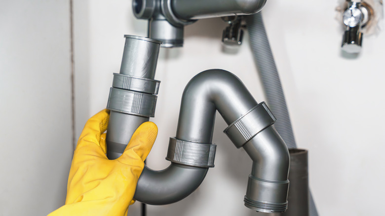 A person's gloved hand fixing kitchen pipes