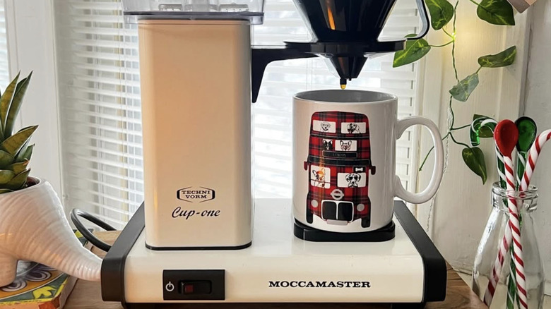 A Moccamaster with a cup on table near a window