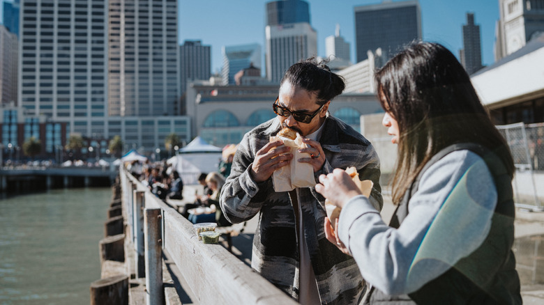 Two people eating food on a pier in San Francisco.