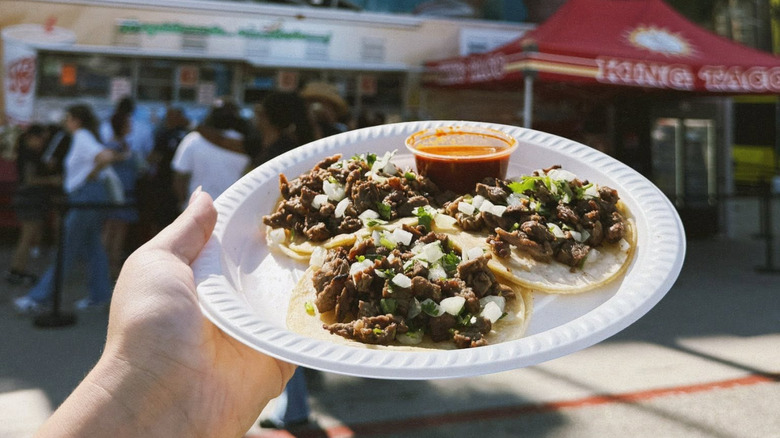 A hand holding a plate of tacos and sauce.
