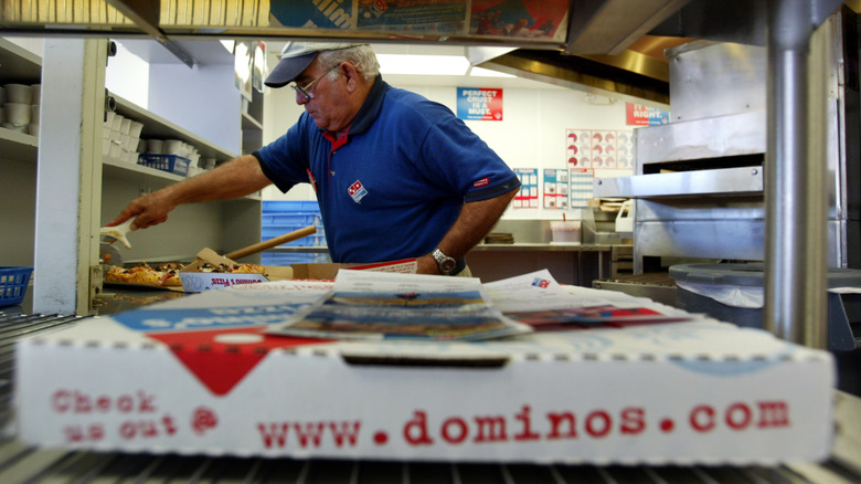 Domino's employee slices a pizza in the background, with a boxed pizza in the foreground