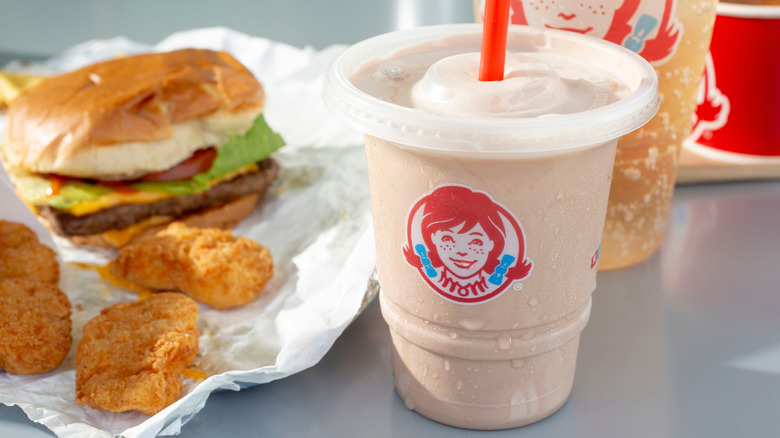 Wendy's frosty, chicken nuggets, cheeseburger, and soft drink set out on a table
