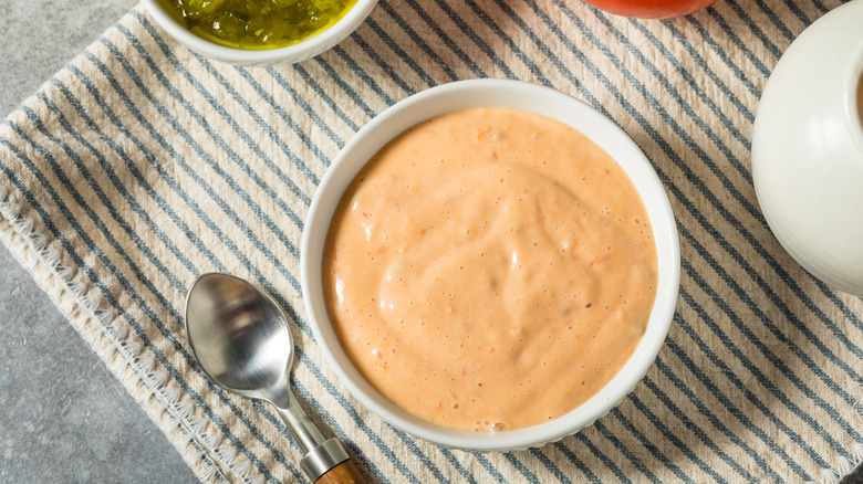A bowl of pink burger sauce on a striped towel, a spoon on the side
