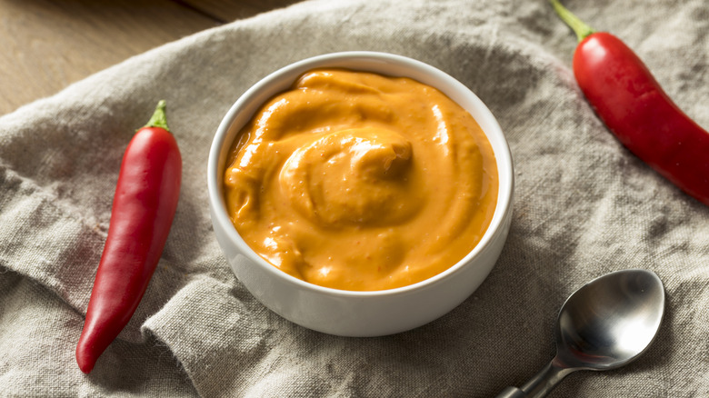 A small white bowl filled with spicy mayo and red peppers on the side