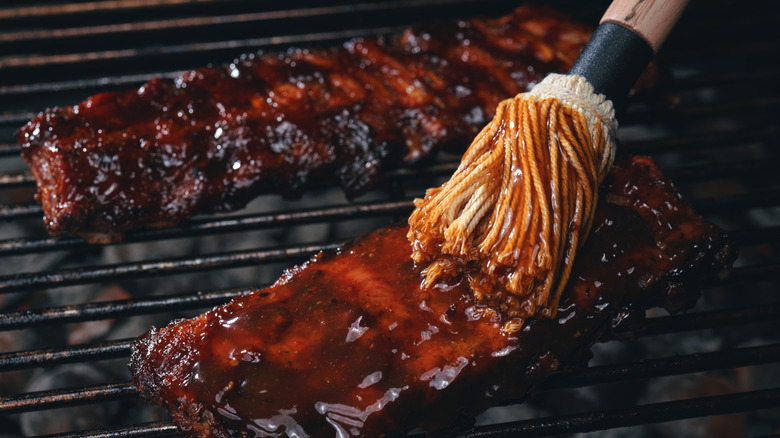 A brush spreads barbecue sauce on ribs on the grill