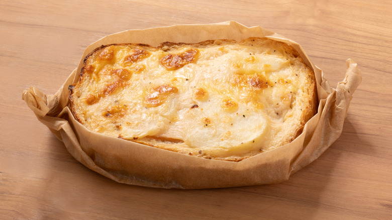 Cheesy, croque monsieur-topped baked potato, wrapped in parchment and sitting on board