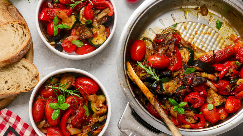 Bowls and pan full of ratatouille French vegetable stew, next to sliced bread