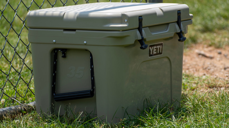 A Yeti cooler sits in the grass near a fence