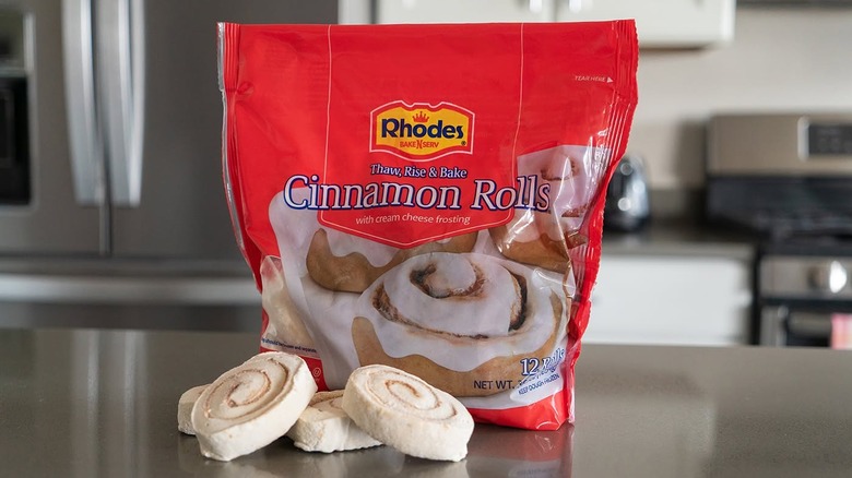 A bag of Rhodes frozen cinnamon rolls sitting on a counter in front of some loose, unbaked rolls