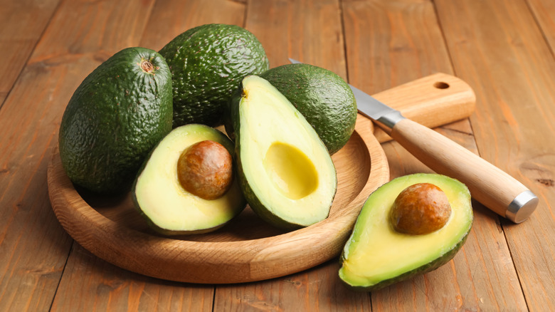 Avocados on a wooden surface, some whole and some cut