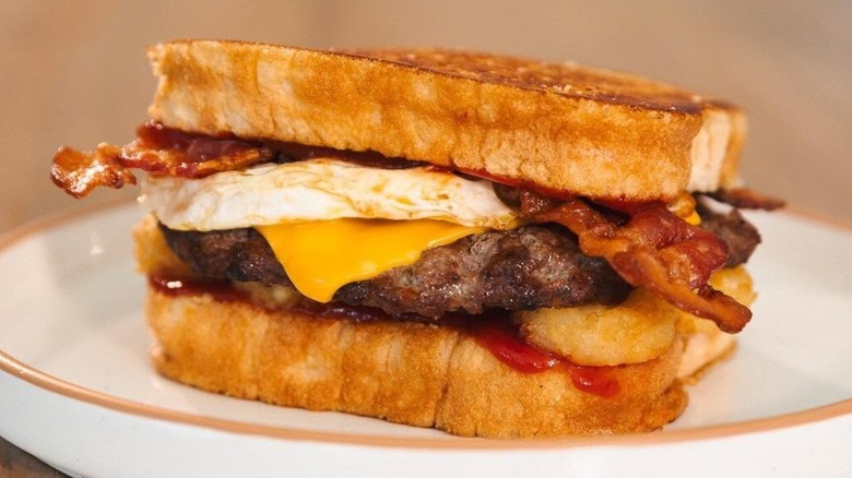 A Hardee's Frisco Breakfast Burger featuring a burger patty, cheese, bacon, and egg on toast.