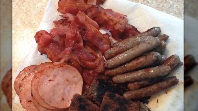 Fried bacon, sausage, and ham on a paper towel.