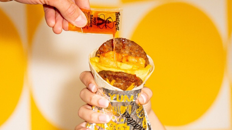 A pack of Texas Pete Hot Sauce being emptied into a Hardee's breakfast burrito.