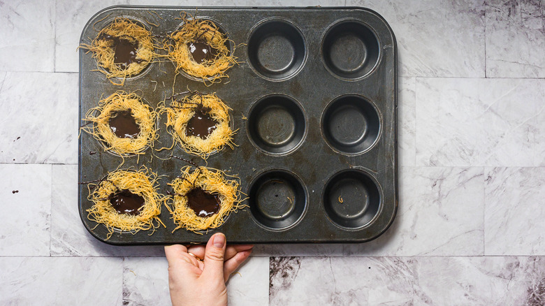 Holding muffin tin with kataifi noodle nests filled with chocolate