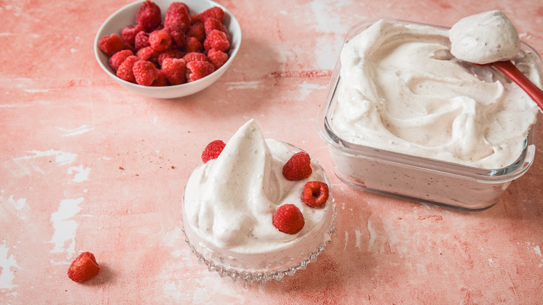 Raspberry marshmallow fluff in glass container with fresh raspberries.