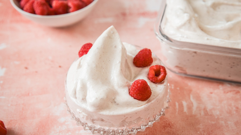 Close up on raspberry marshmallow fluff in glass container with fresh raspberries