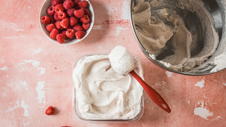 Raspberry marshmallow fluff in glass container with fresh raspberries beside large metal bowl