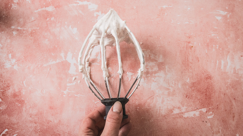 Hand holding whisk with stable raspberry marshmallow fluff on it