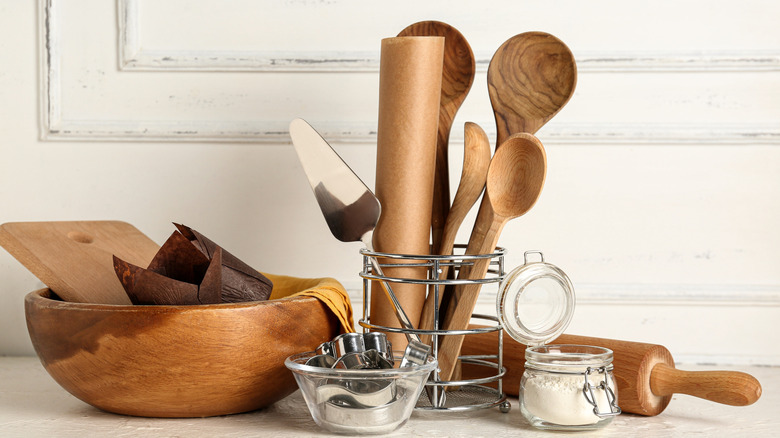Utensil steel jar with several wooden spoons next to a wooden bowl, containers, and a rolling pin