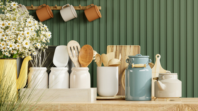 Pretty countertop decor with pots, flower, and utensils against green paneled walls