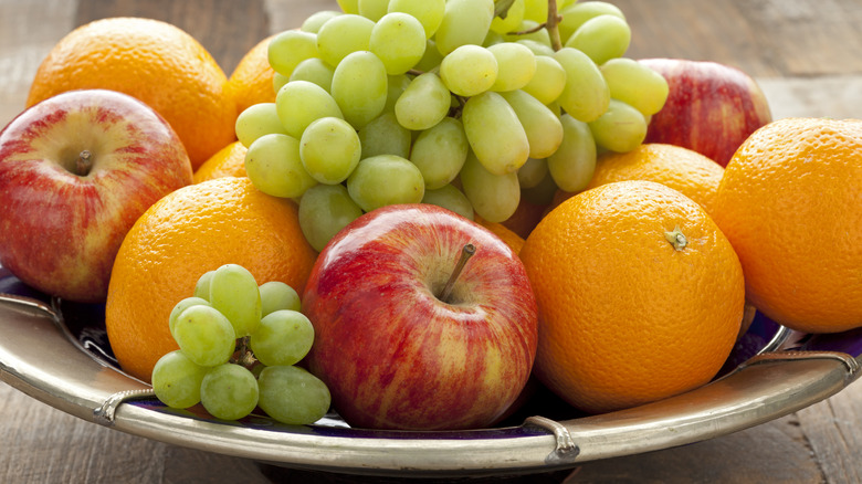 Fresh fruits including apples, oranges, and grapes arranged in a bowl on a table