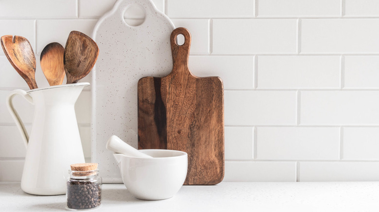 Wooden cutting board and other countertop essentials arranged in an all-white kitchen
