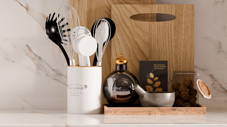 Wooden tray with kitchen essentials placed next to utensil jar and wooden chopping boards