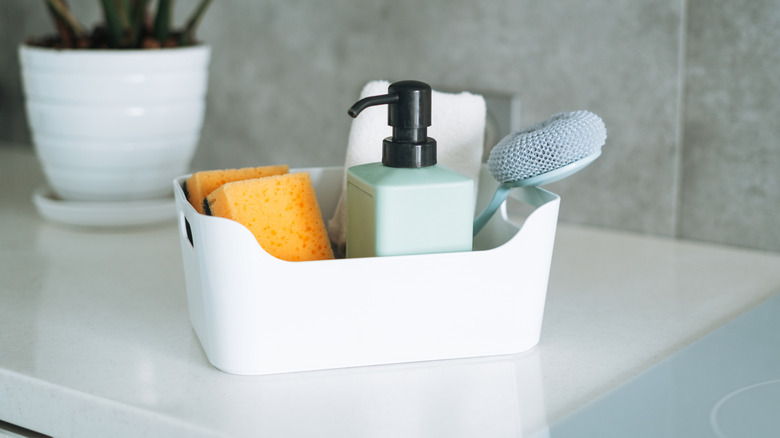 Kitchen cleaning supplies arranged in a caddy on a white countertop