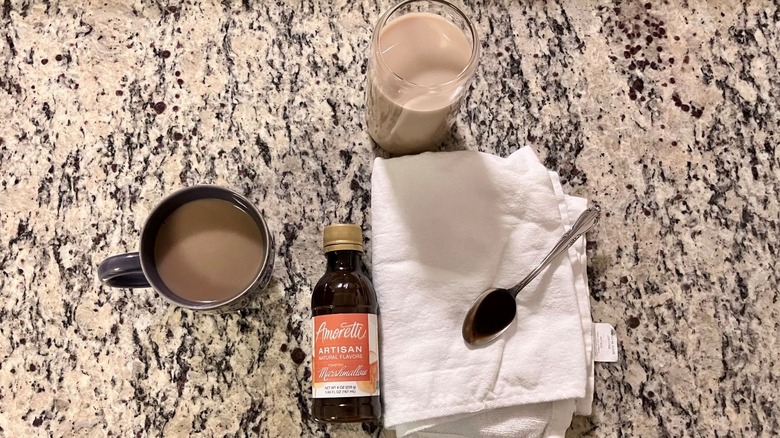 A bottle of Amoretti Natural Toasted Marshmallow Artisan Flavor sits in the center of a hot coffee, an iced coffee, and a spoonful of syrup