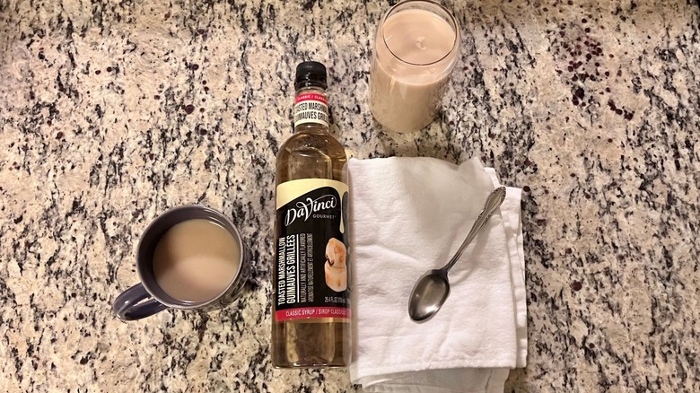 A bottle of DaVinci Gourmet Classic Toasted Marshmallow Syrup sits in the center of a hot coffee, an iced coffee, and a spoonful of syrup