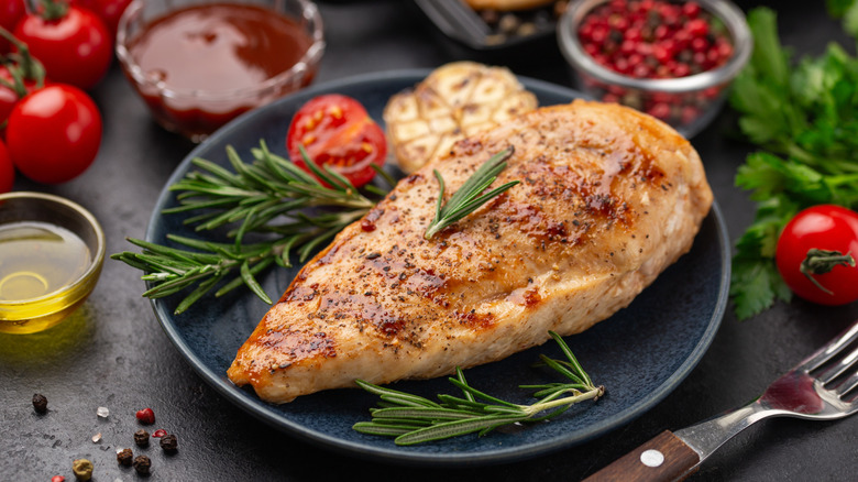 A grilled chicken breast on a plate with rosemary garnish