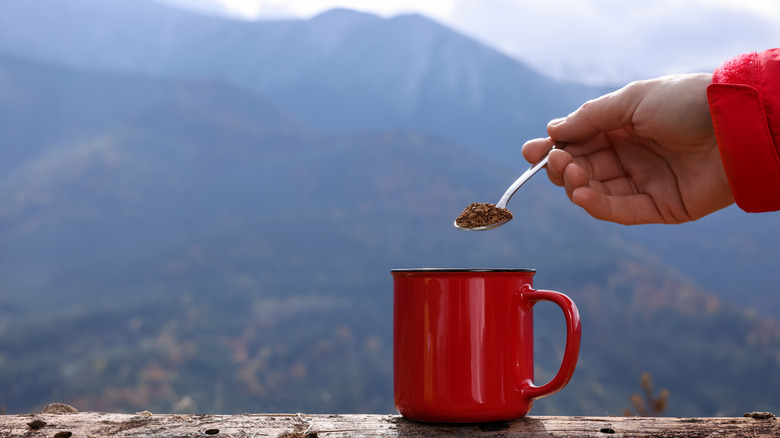 adding instant coffee to mug with mountain background