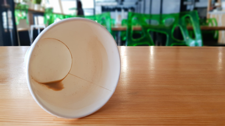 Empty paper coffee cup laying on its side on a wooden table at a coffee shop