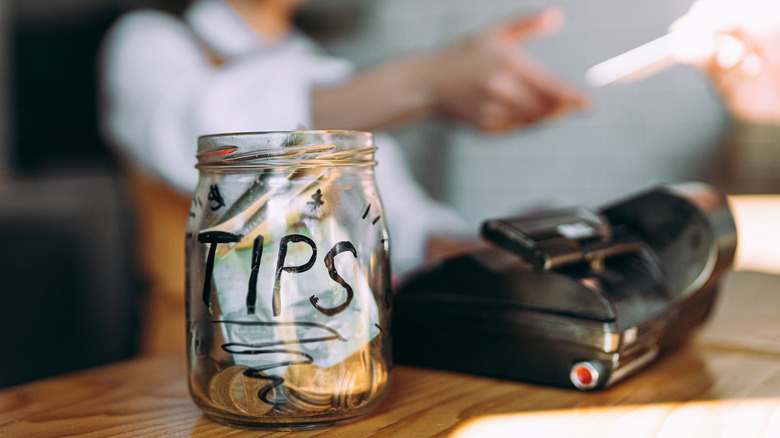 Tip jar in the foreground with a customer paying the barista in the background