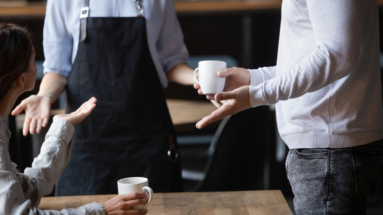 Two coffee shop customers and a barista arguing