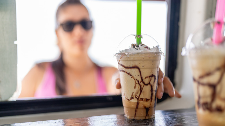Person grabbing frozen coffee drink topped with whipped cream