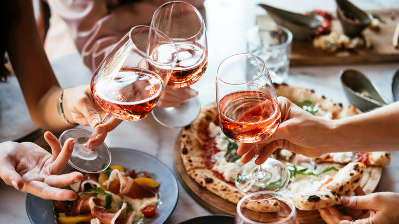 Friends toasting with glasses of wine over a restaurant table with pizza and food
