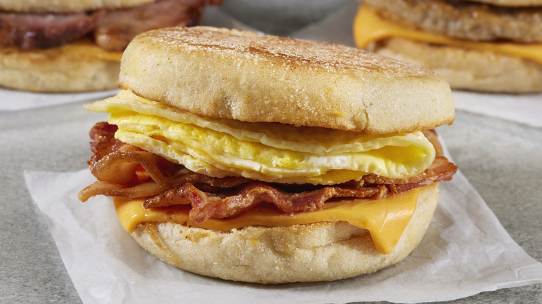 English muffin breakfast sandwich with bacon, egg, and cheese sitting on white wax paper wrapping