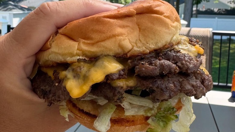A person's hand holding a cheeseburger from Crowley's Dive Bar