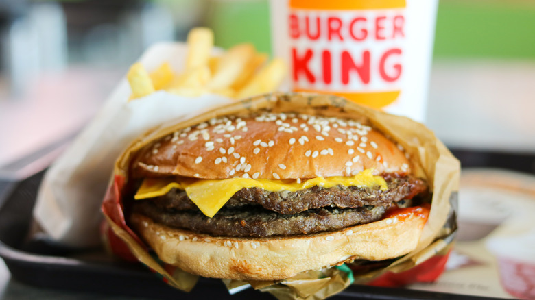 A half-wrapped double cheeseburger on a tray with fries and a Burger King cup in the background