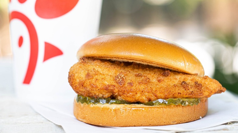 An original Chick-fil-A Chicken Sandwich on a table, with a soda cup in the background